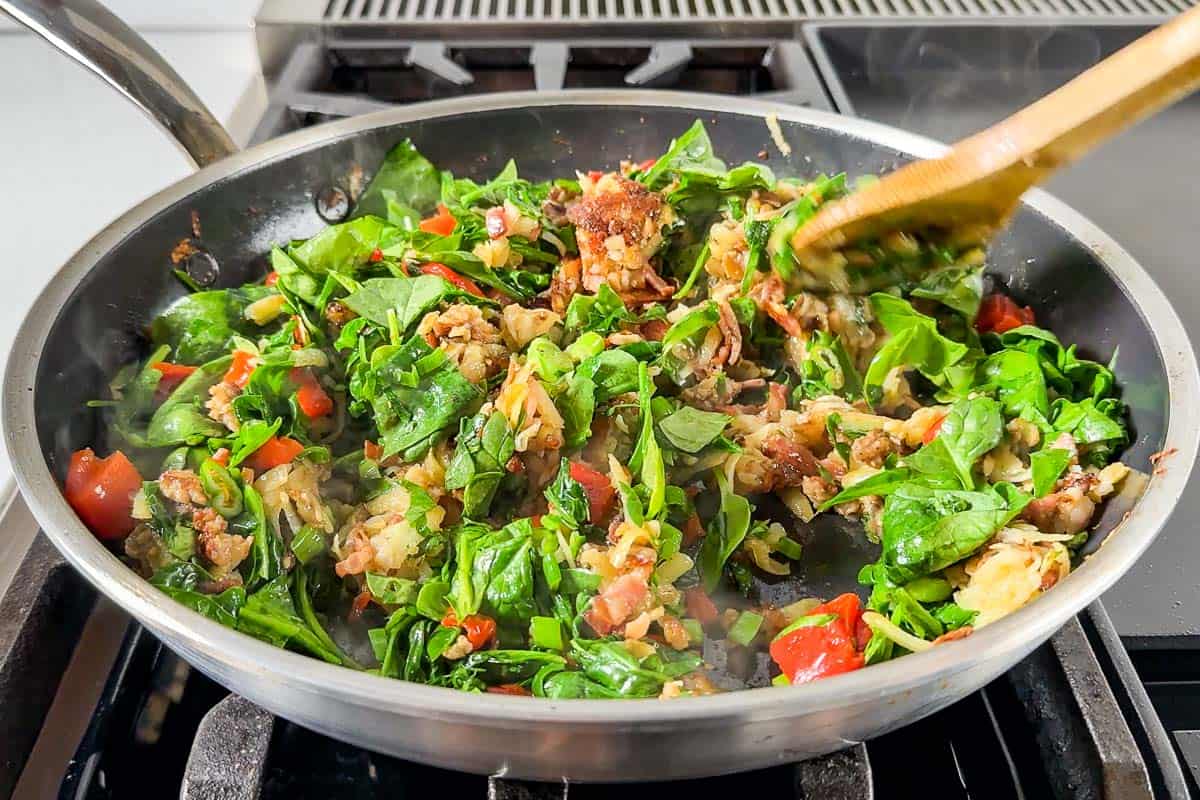 Adding the spinach, green onions, and bell pepper to the pan with the hash browns, sausage, and bacon.