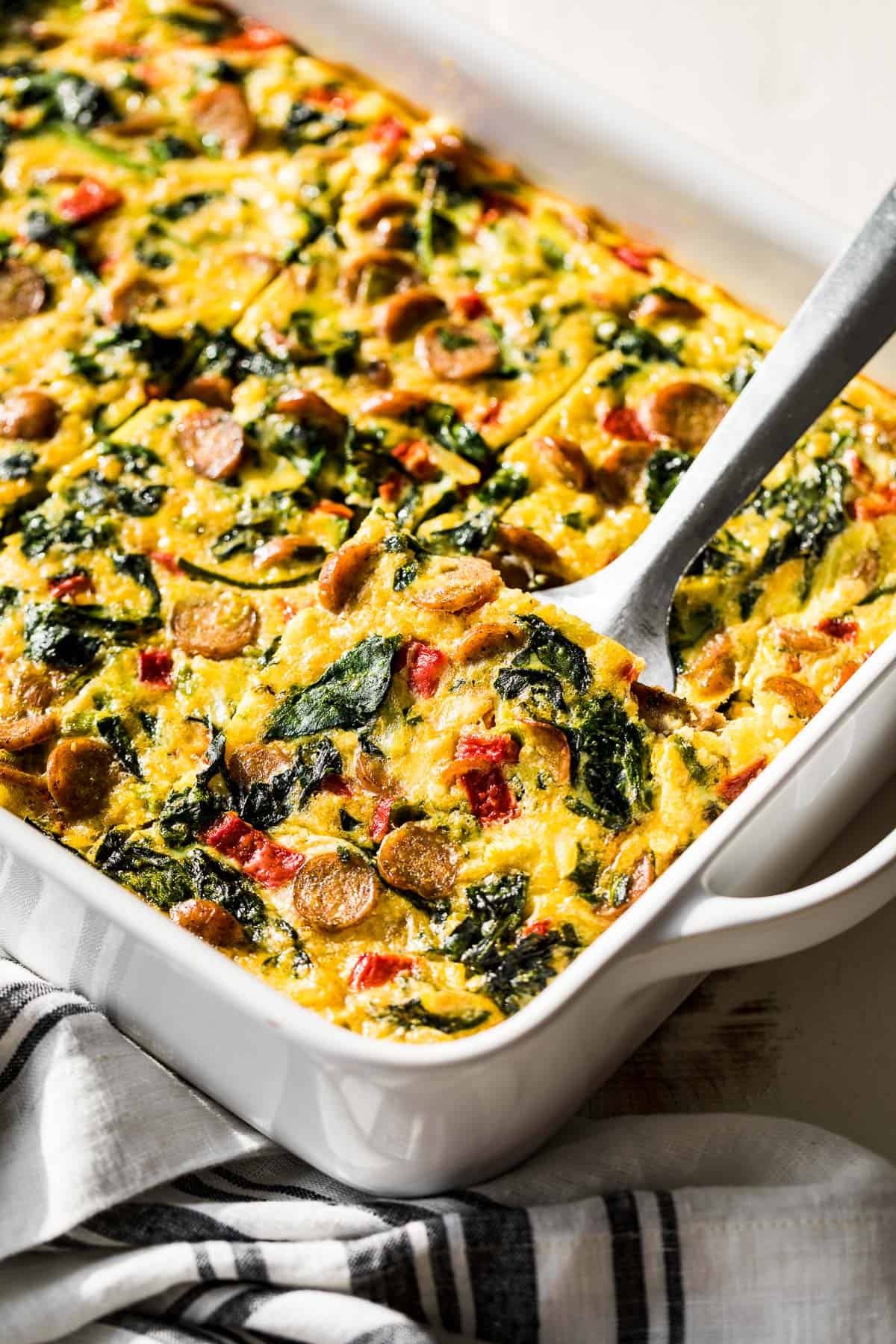 Breakfast Casserole in a large white baking dish with a metal spatula scooping up one slice.