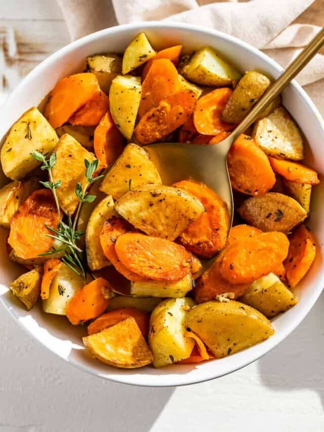 Cubed roasted carrots and potatoes in a white bowl with a gold spoon.