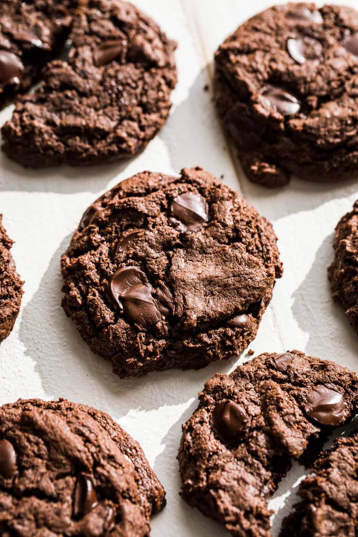 Chocolate almond butter cookies on a white background with one cookie broken in half.