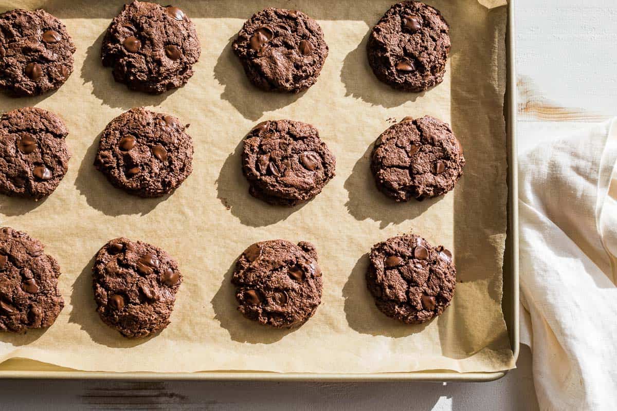 Baked chocolate almond butter cookies on a parchment lined baking sheet.