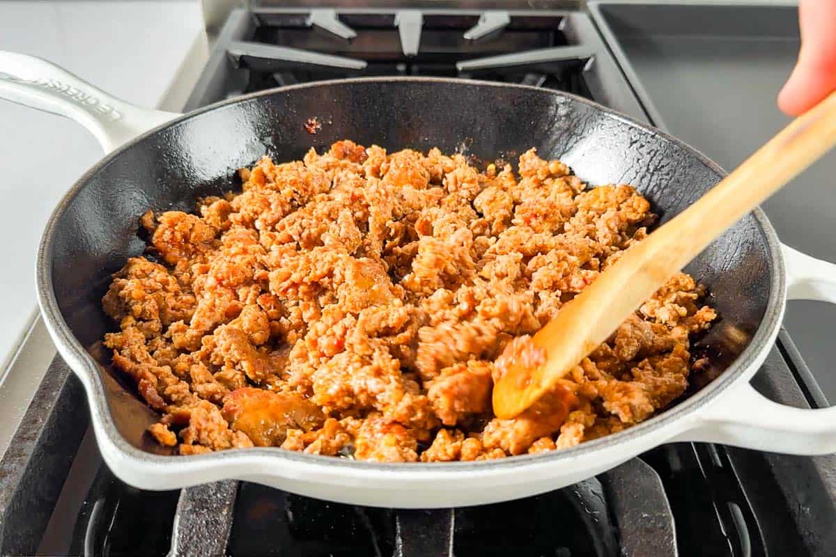 Sautéing chorizo pasta in a large white skillet on a stove top.