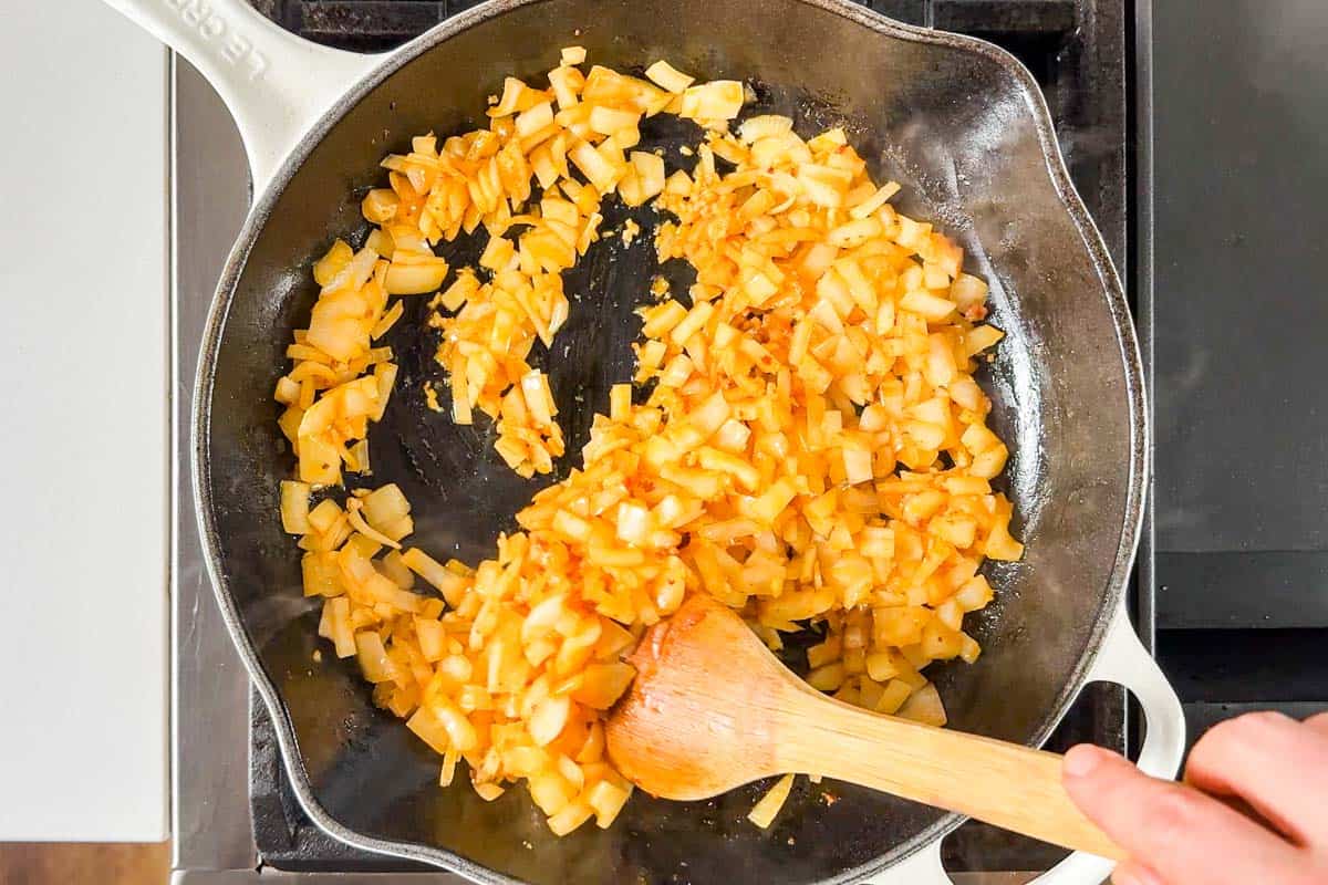 Cooking the onions and garlic in a large white skillet on the stove top.