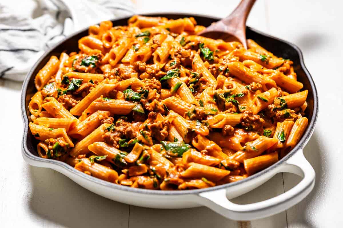 Large white skillet filled with chorizo pasta with a wood spoon in the side of the skillet.