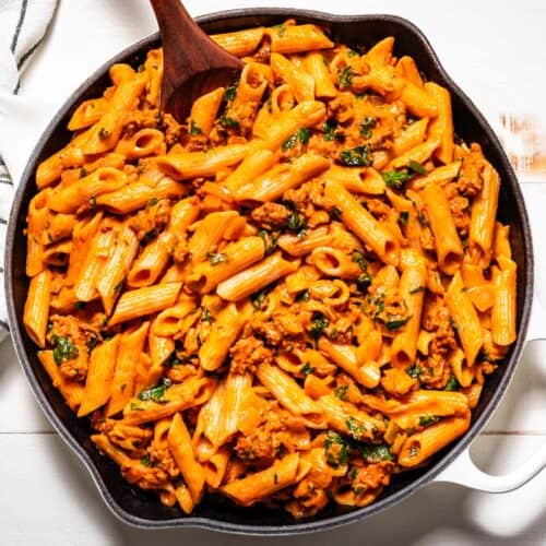 Finished chorizo pasta in a large white skillet with a black and white linen on the side of the dish.