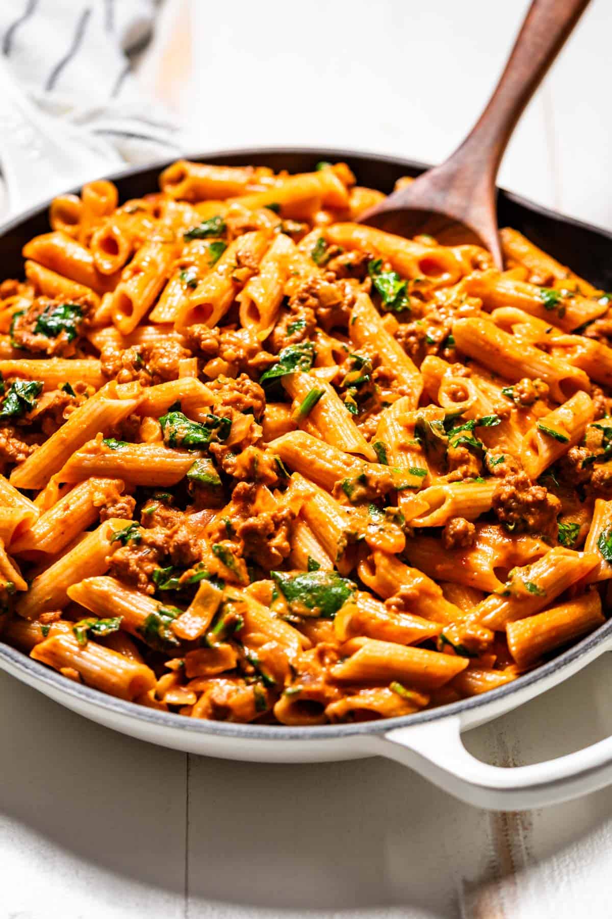 Chorizo pasta with cooked spinach and a wood spoon in the side of the pasta in a white skillet.