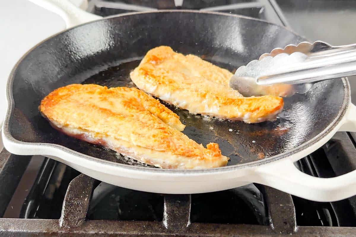 Searing the chicken breasts in a large white skillet on the stovetop.