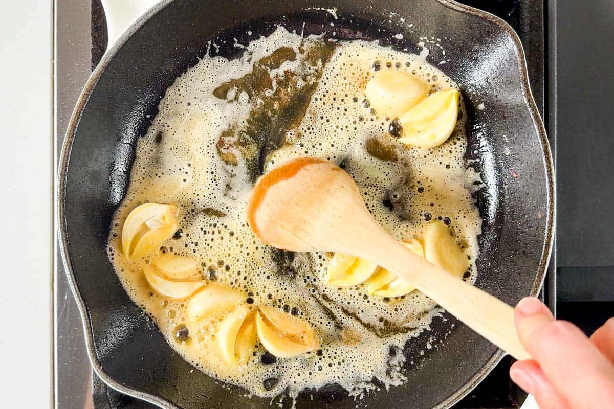 Cooking the halved garlic cloves in butter in a large white skillet.
