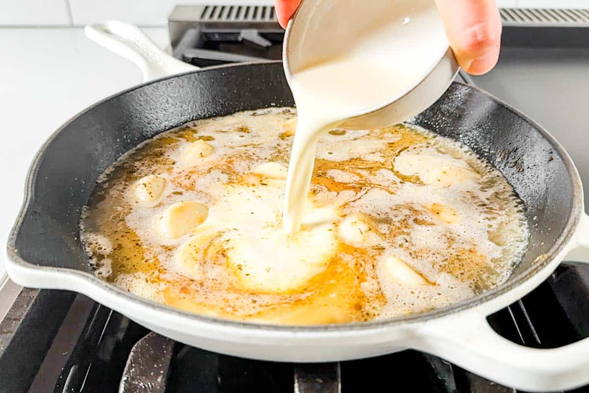 Adding the chicken broth and cream to the white skillet on the stovetop.