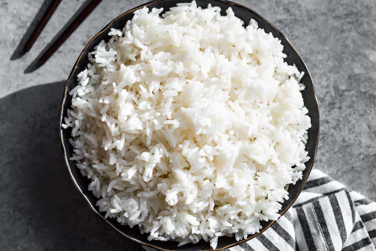 Finished cooked rice in a black bowl with chopsticks on the side and a black and white striped linen on the other side of the bowl.