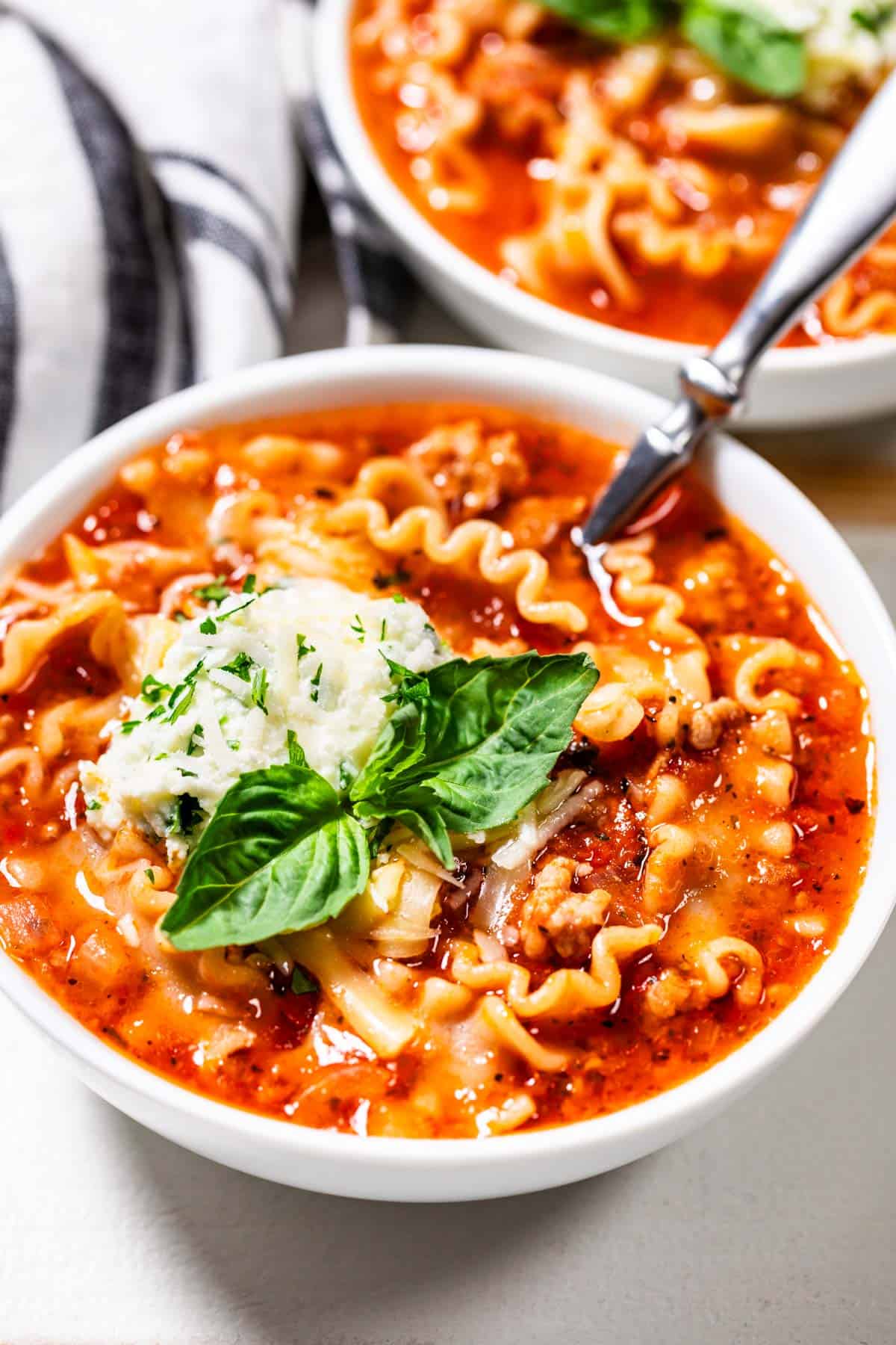 Lasagna Soup in a white bowl with a green basil garnish on top.