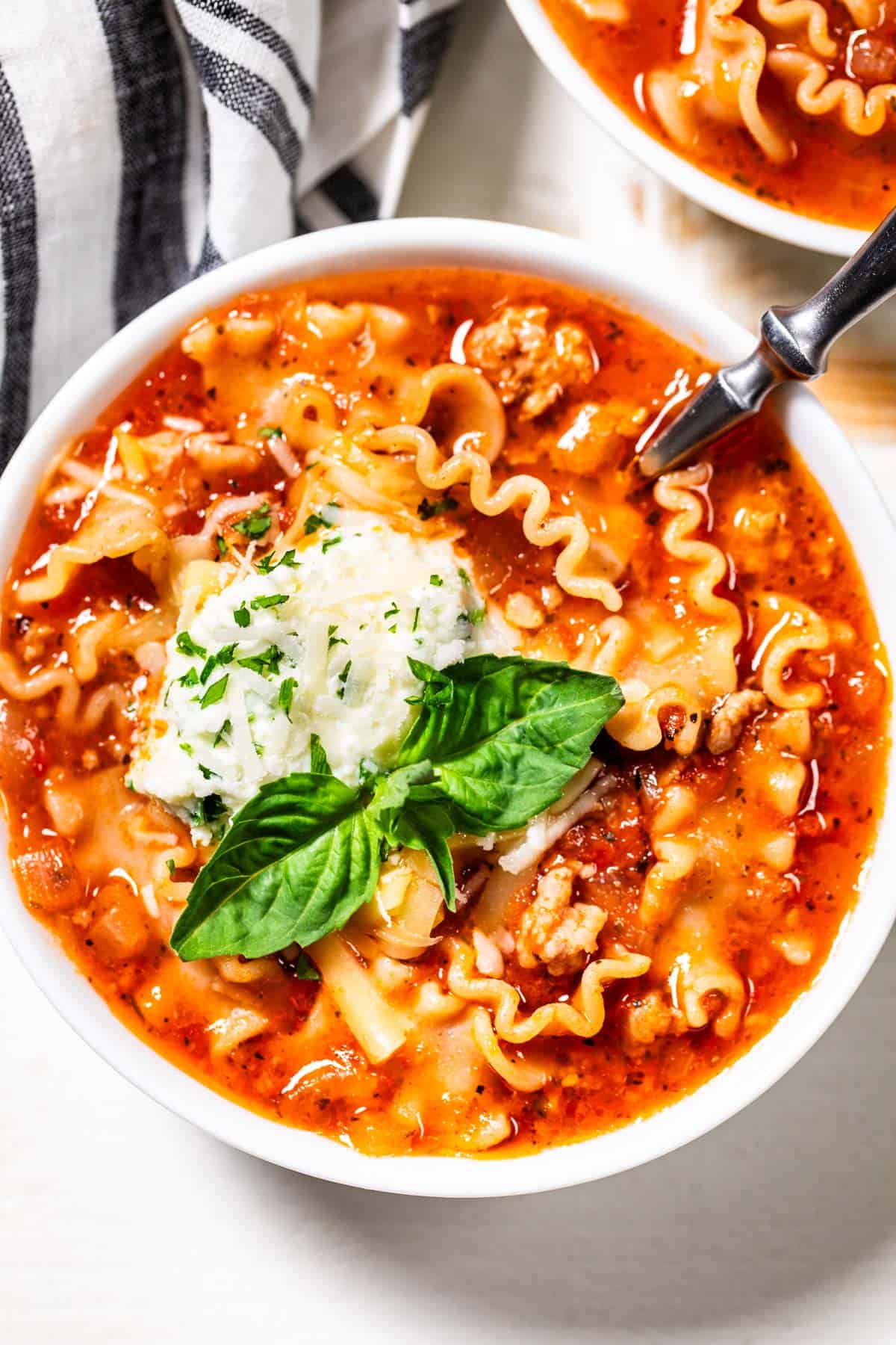 Lasagna Soup in a white bowl topped with fresh herbs and cheese.