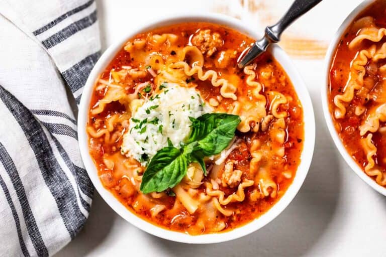 Lasagna soup in two white bowls with a spoon in the soup topped with cheese and fresh basil.