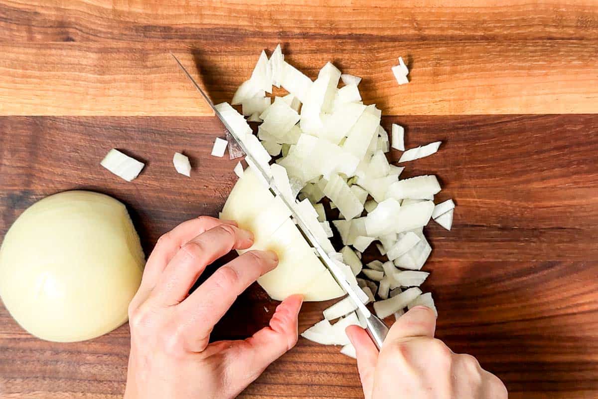 Dicing an onion with a chef's knife on a wood cutting board.