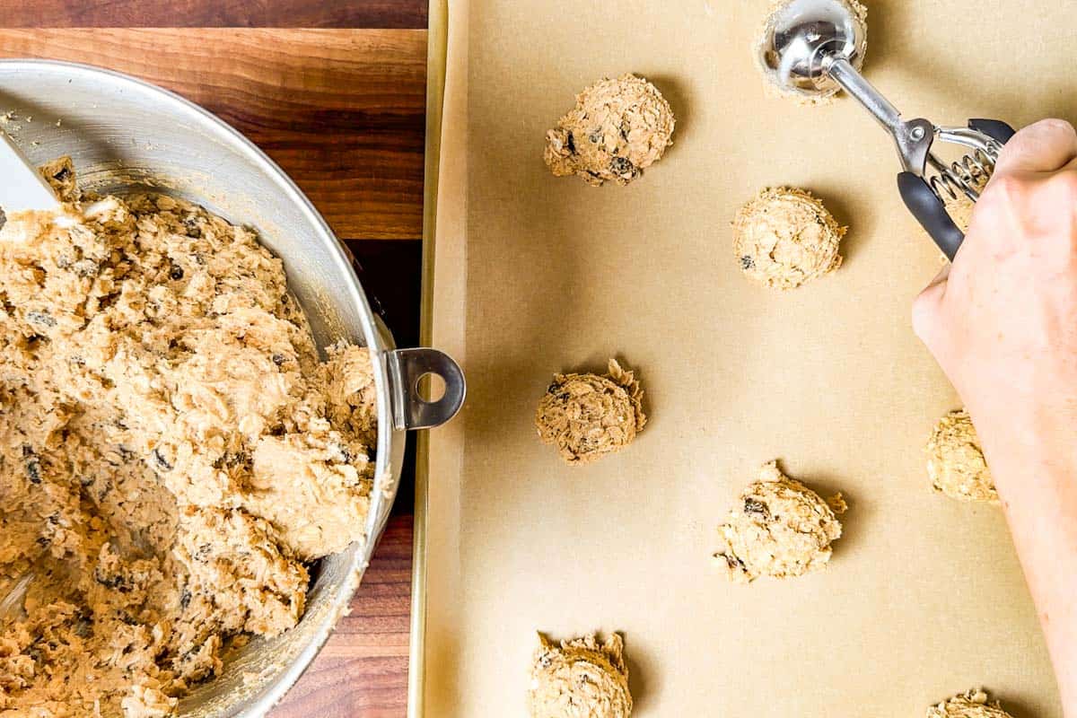 Portioning out the cookie dough with a metal cookie scoop onto a parchment lined baking sheet.