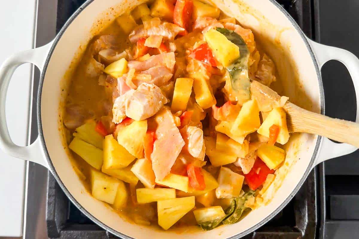 Adding the pineapple to the curry and stirring it together.