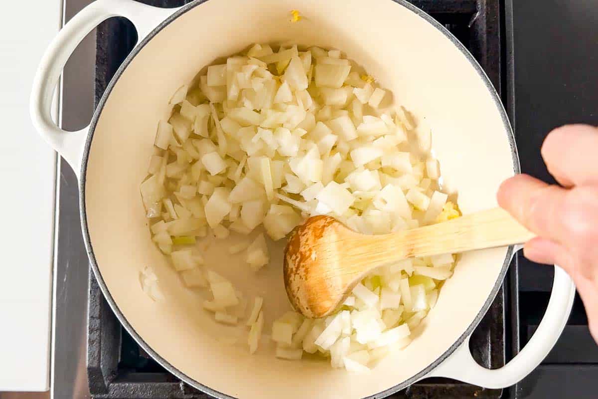 Cooking the onion and garlic in a large white pot on the stovetop.