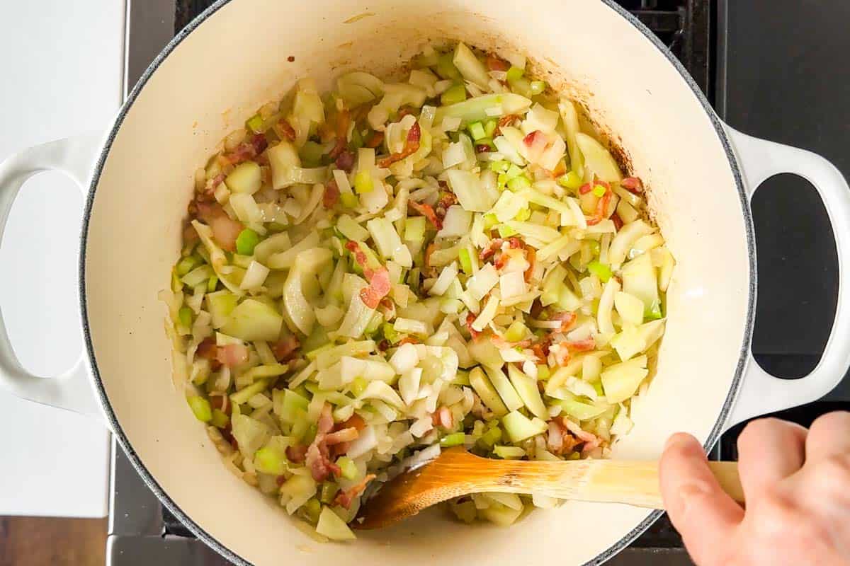 Chopped celery, fennel, and onion added to the cooking bacon in a large white Dutch oven.