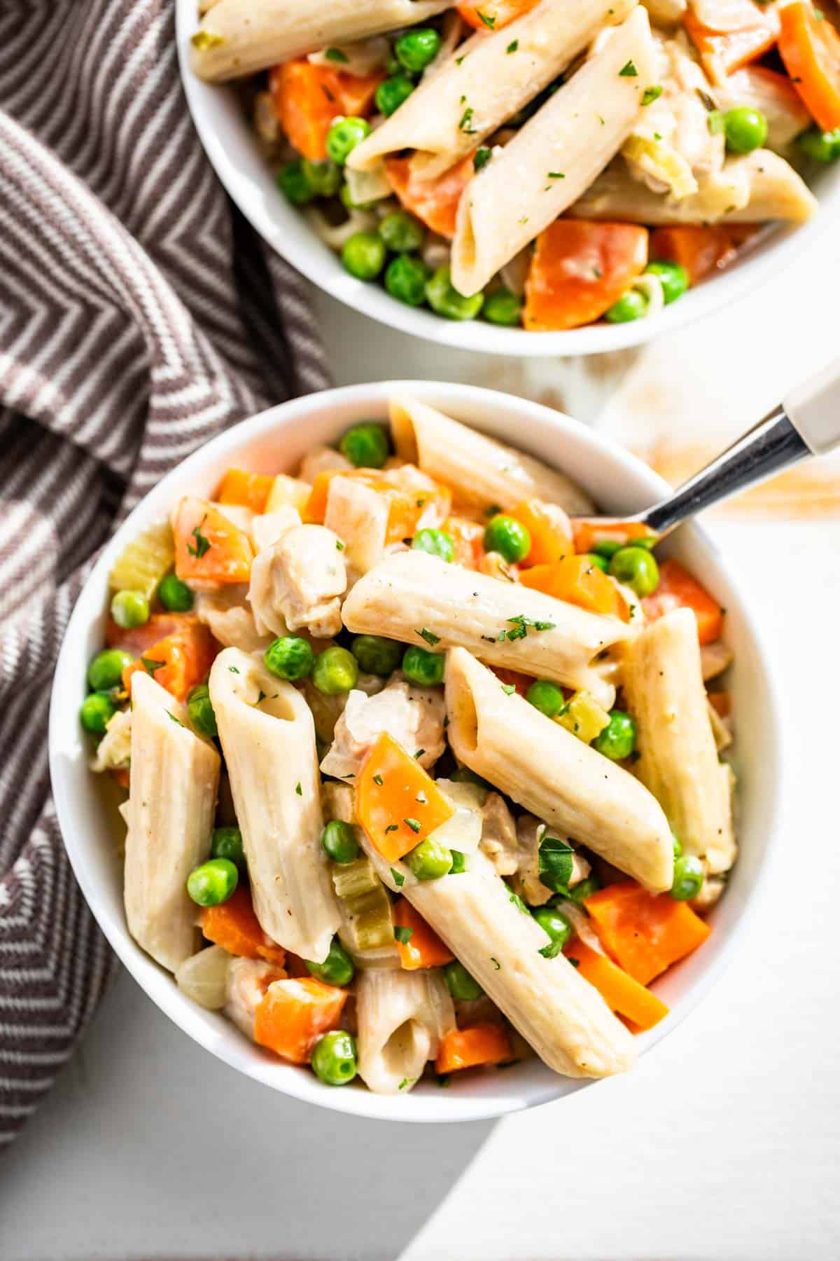 Two bowls of chicken pot pie pasta on a white background with a white handled fork in one bowl.