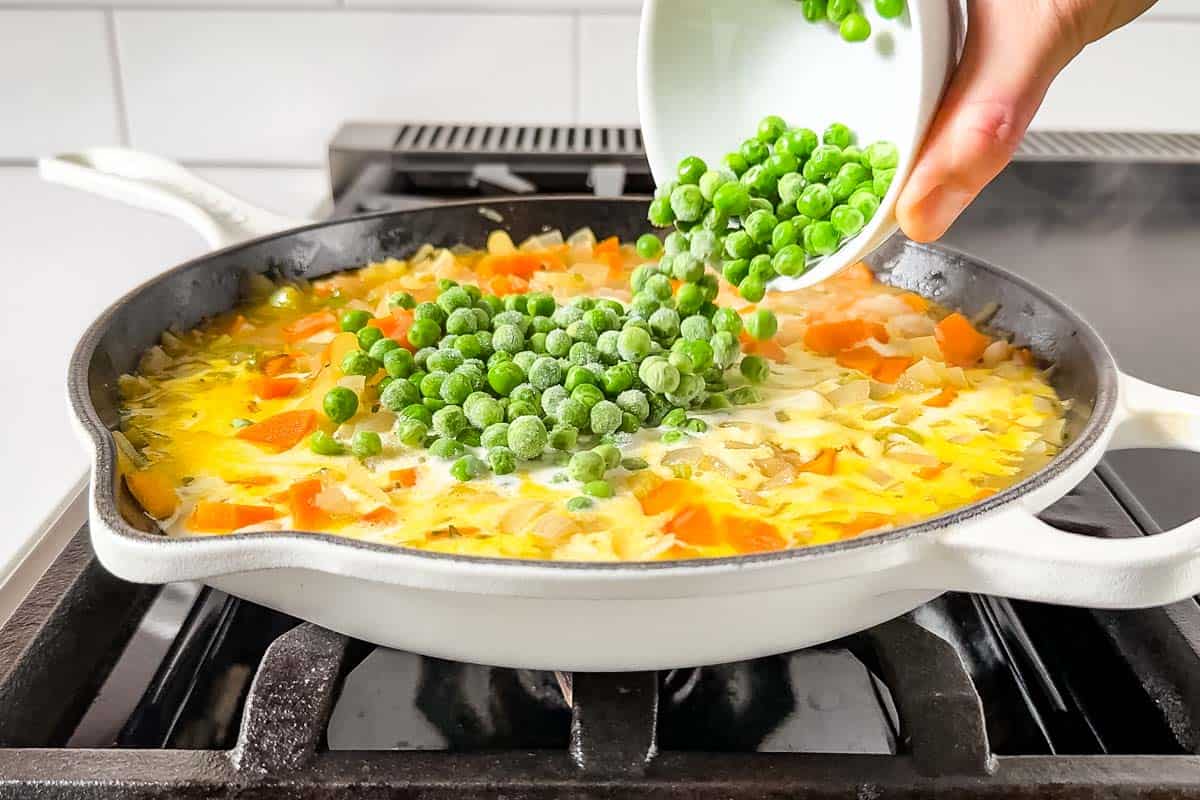 Adding the peas and cooked chicken to the chicken pot pie soup base in the large white skillet.