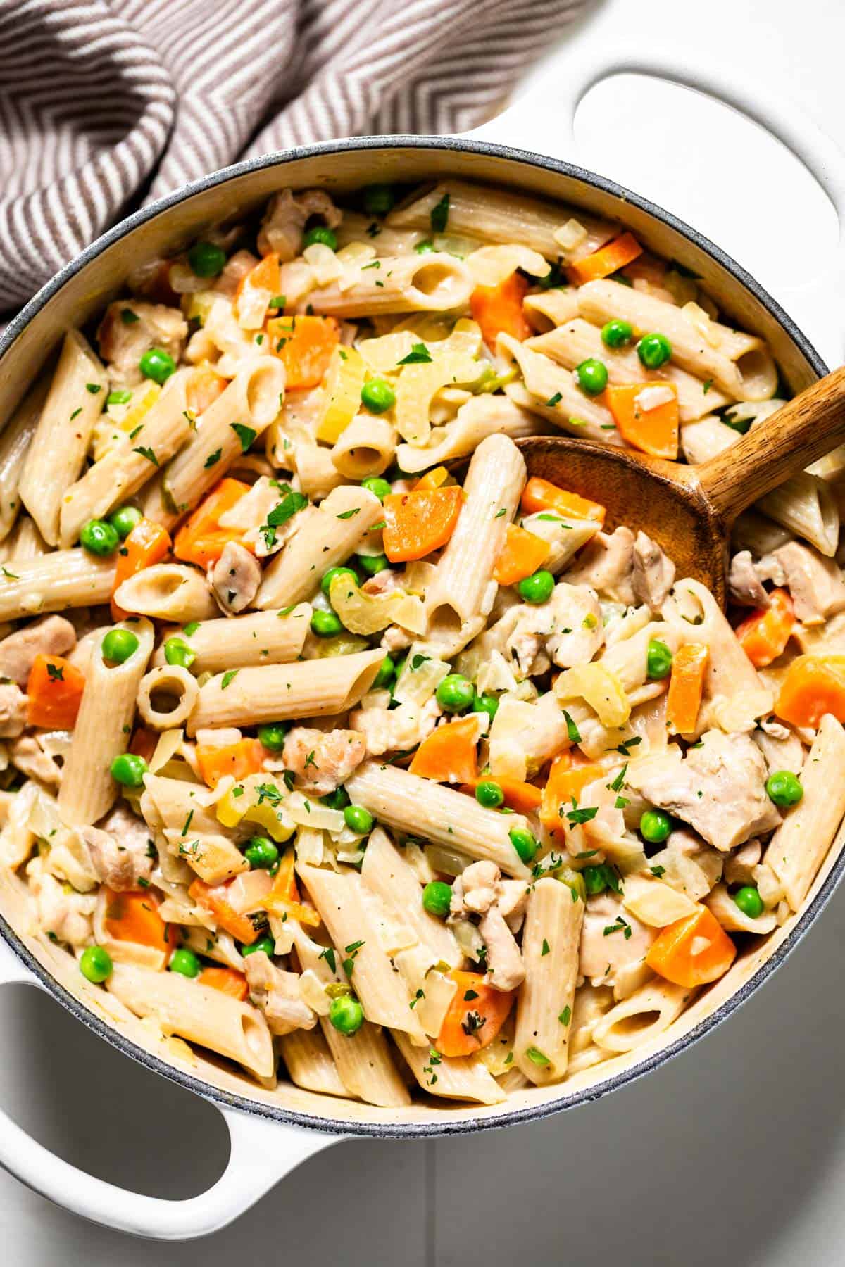 A large white pot filled with chicken pot pie pasta with a wood spoon in it.