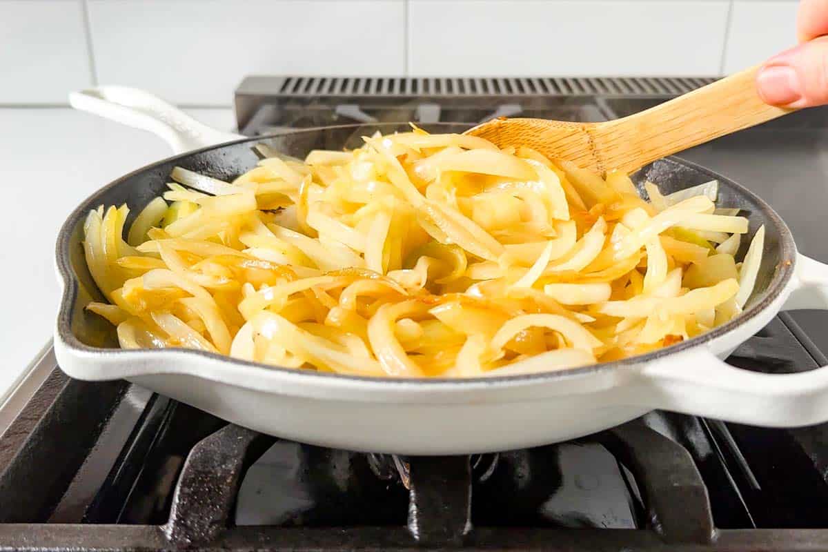 The beginning stages of cooking the onions in a large white skillet turning golden.