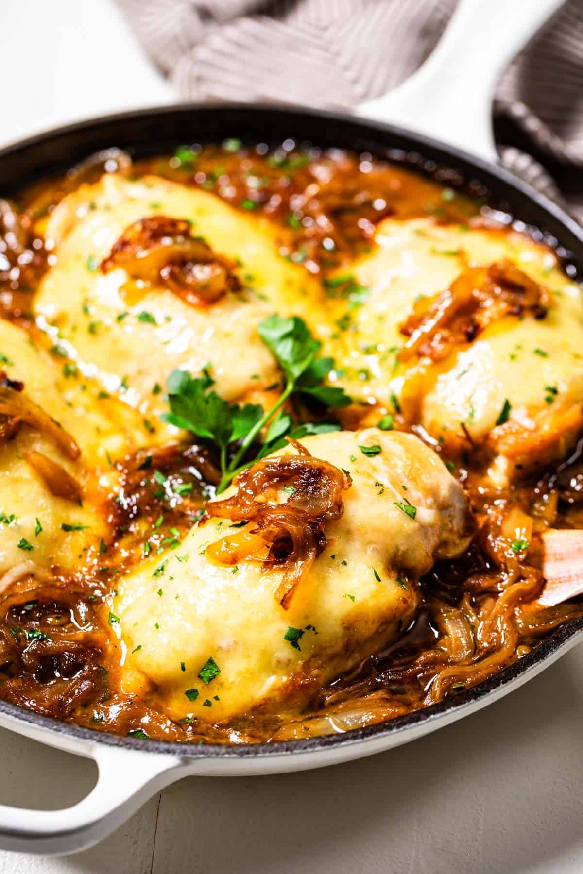 French Onion Chicken being lifted out of the skillet with a wood spatula topped with chopped parsley.