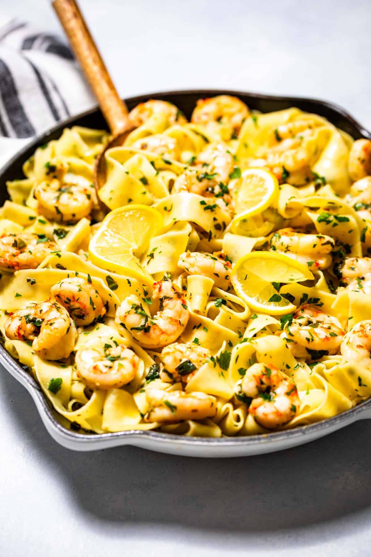 Garlic butter shrimp pasta in a large white skillet topped with lemon slices and chopped parsley.