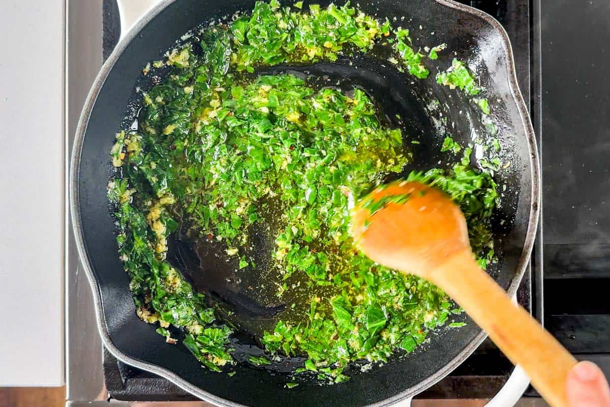 Sautéing garlic and spinach in butter in a white skillet.