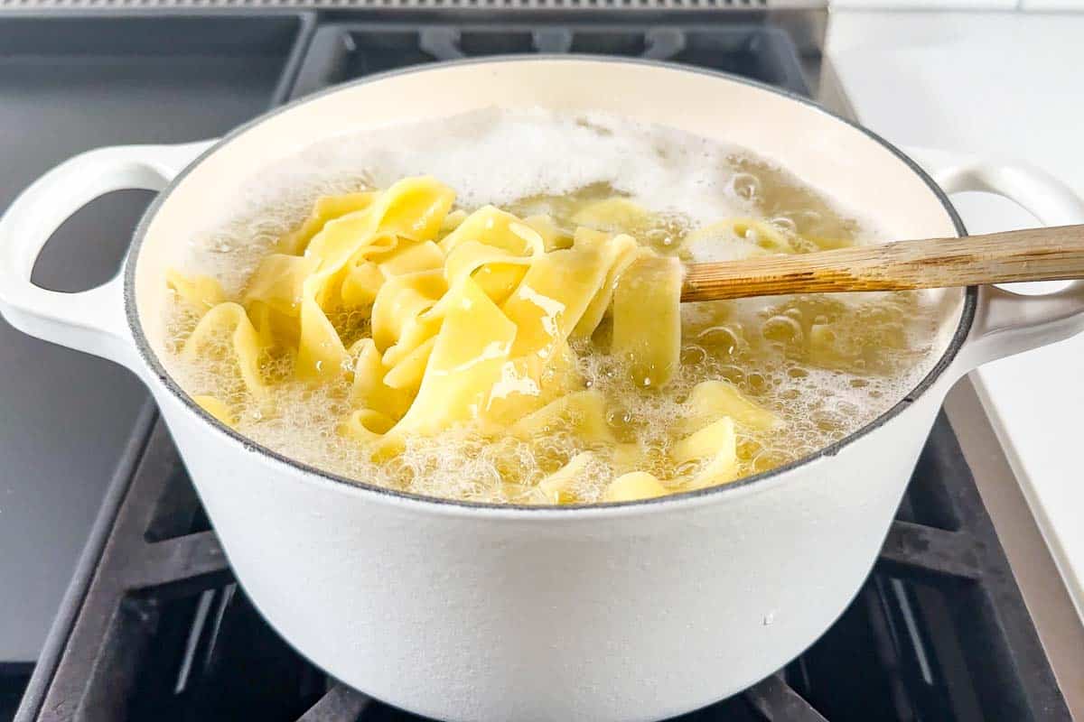 Cooking Pappardelle pasta in a large white pot on the stovetop.