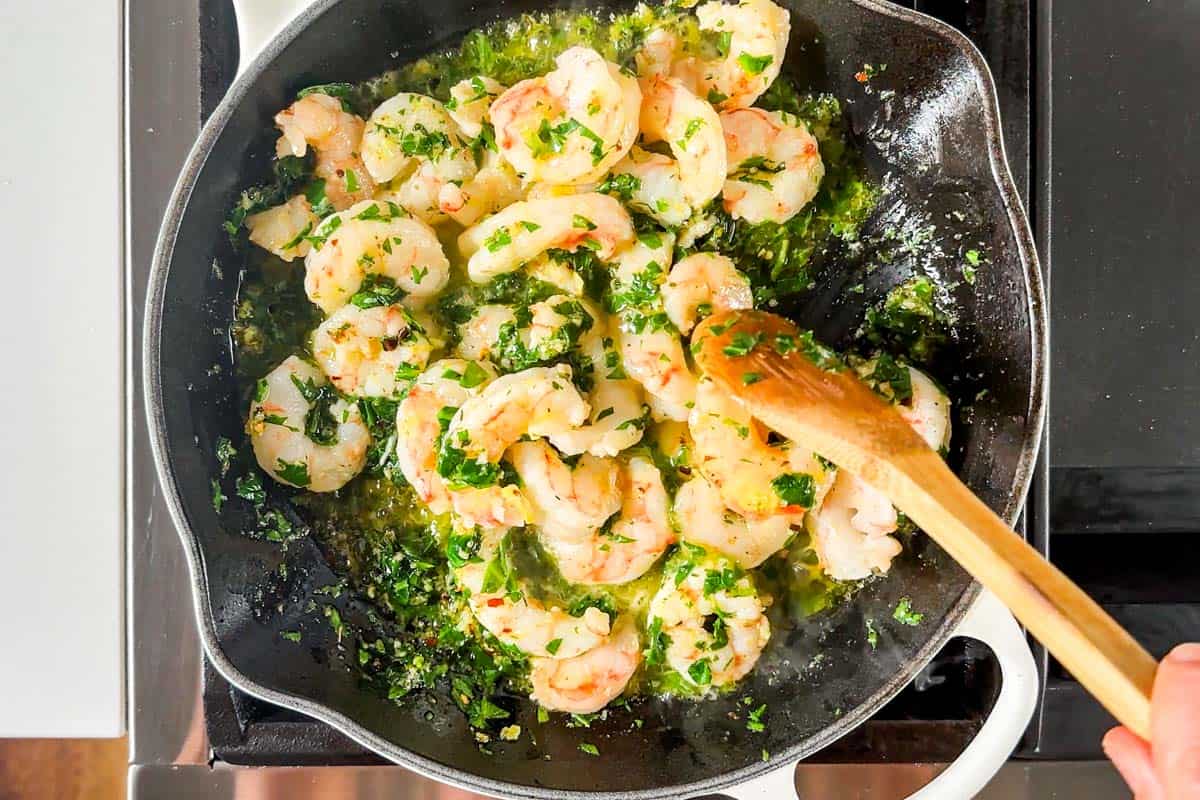 Adding the shrimp to the garlic butter spinach mixture in a large white skillet.