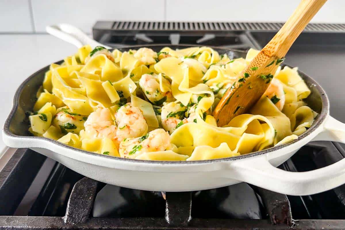 Stirring the pasta together with the garlic butter shrimp mixture in a large white skillet.