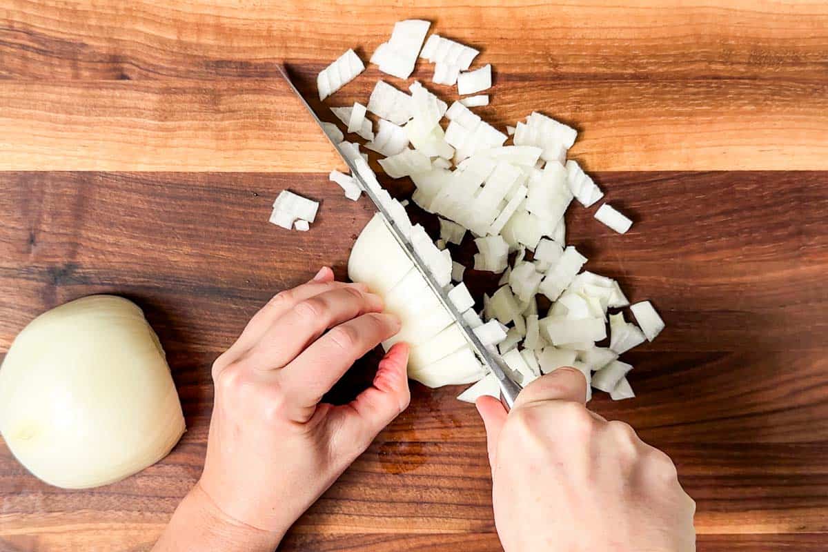 Dicing an onion with a chef's knife on a wood cutting board.