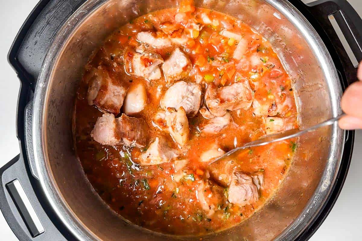 Adding the browned pork shoulder cubes to the tomato mixture in the Instant Pot.