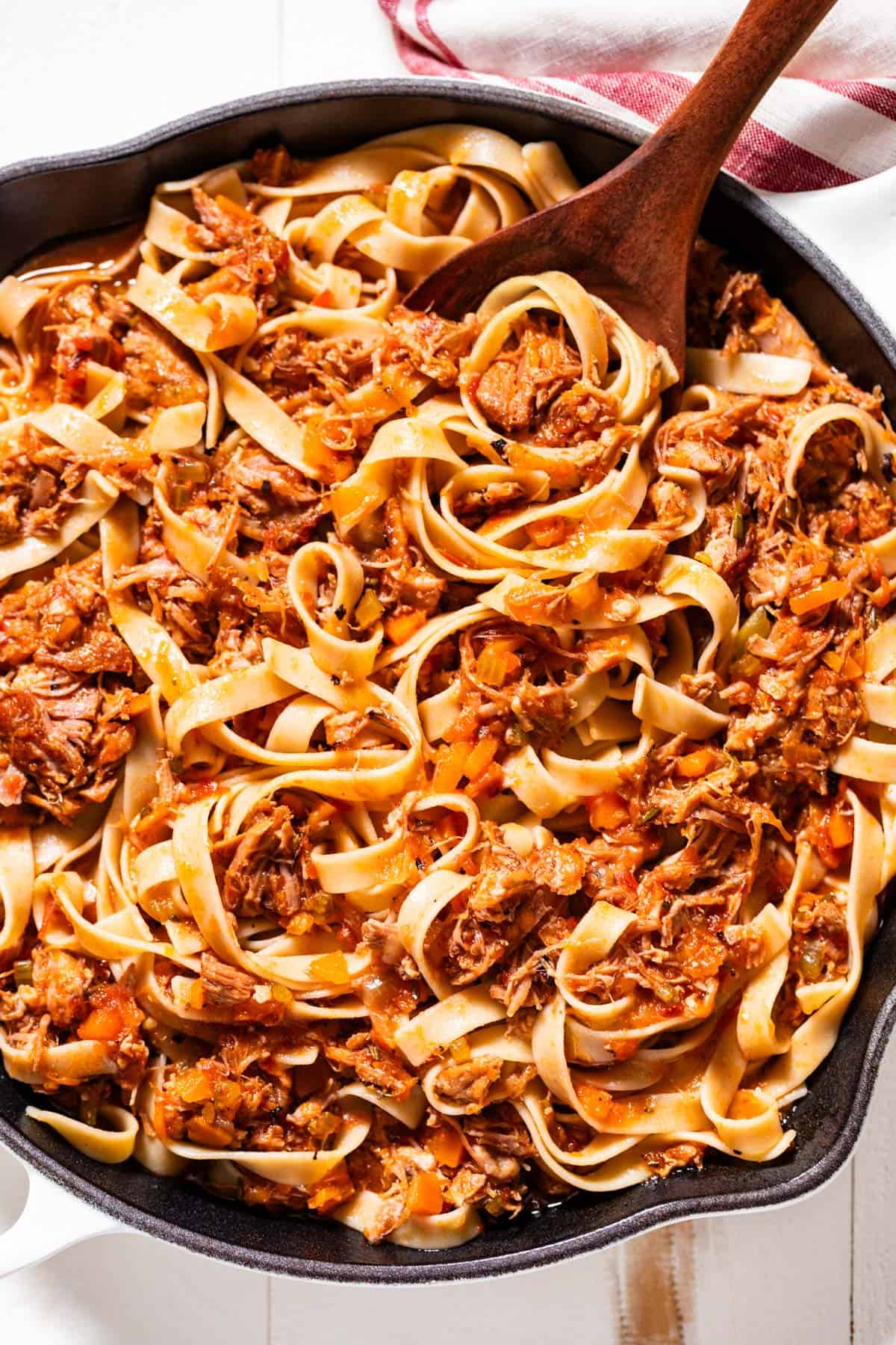 Pork ragu tossed together with tagliatelle pasta in a large white skillet.