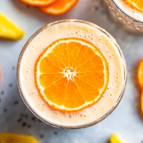 Finished pineapple orange banana smoothie in two glasses topped with orange slices with orange slices around the glasses.
