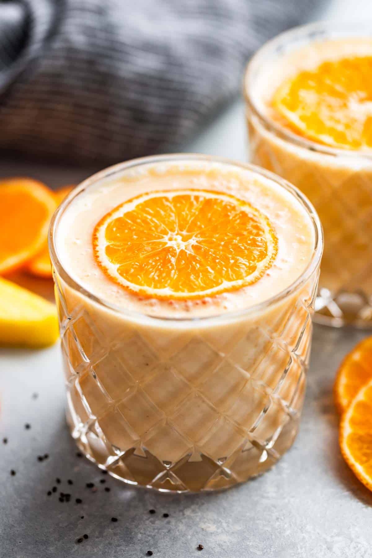 Two glasses of Pineapple Orange Banana Smoothie with orange slices on top and around the glasses.