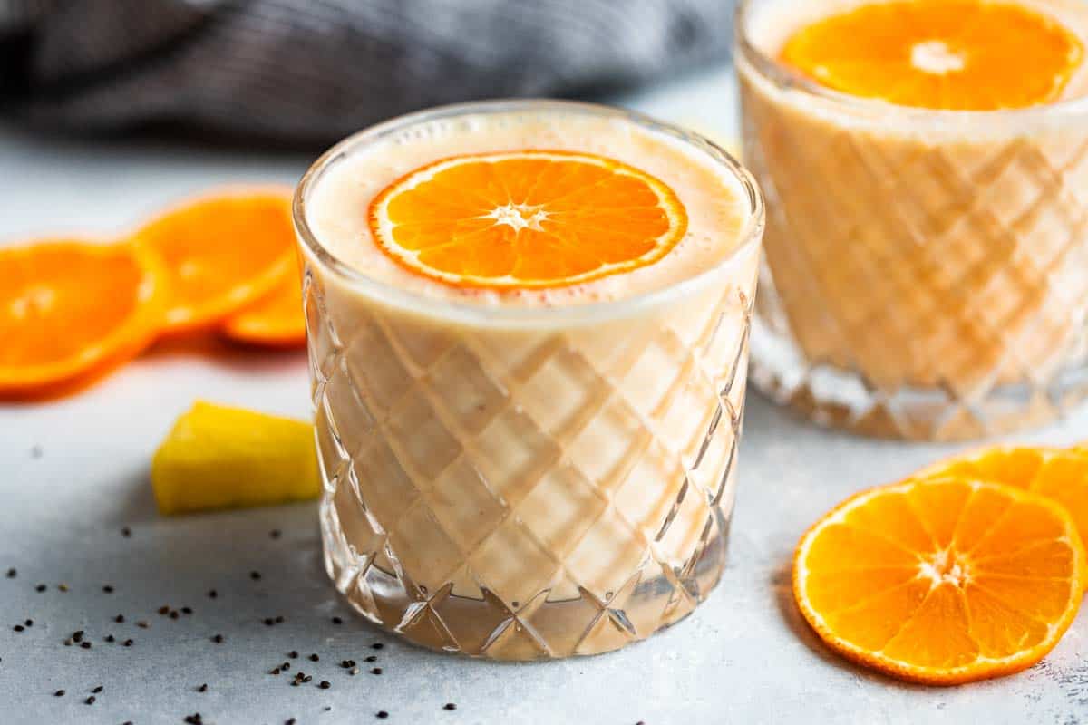 Two glasses of smoothie with orange slices around and a blue linen.