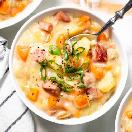 Three white bowls filled with crockpot ham and potato soup with a silver spoon in one bowl.