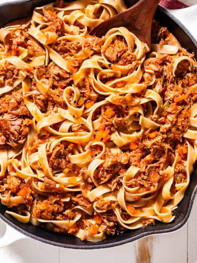 Pork ragu tossed together with tagliatelle pasta in a large white skillet.