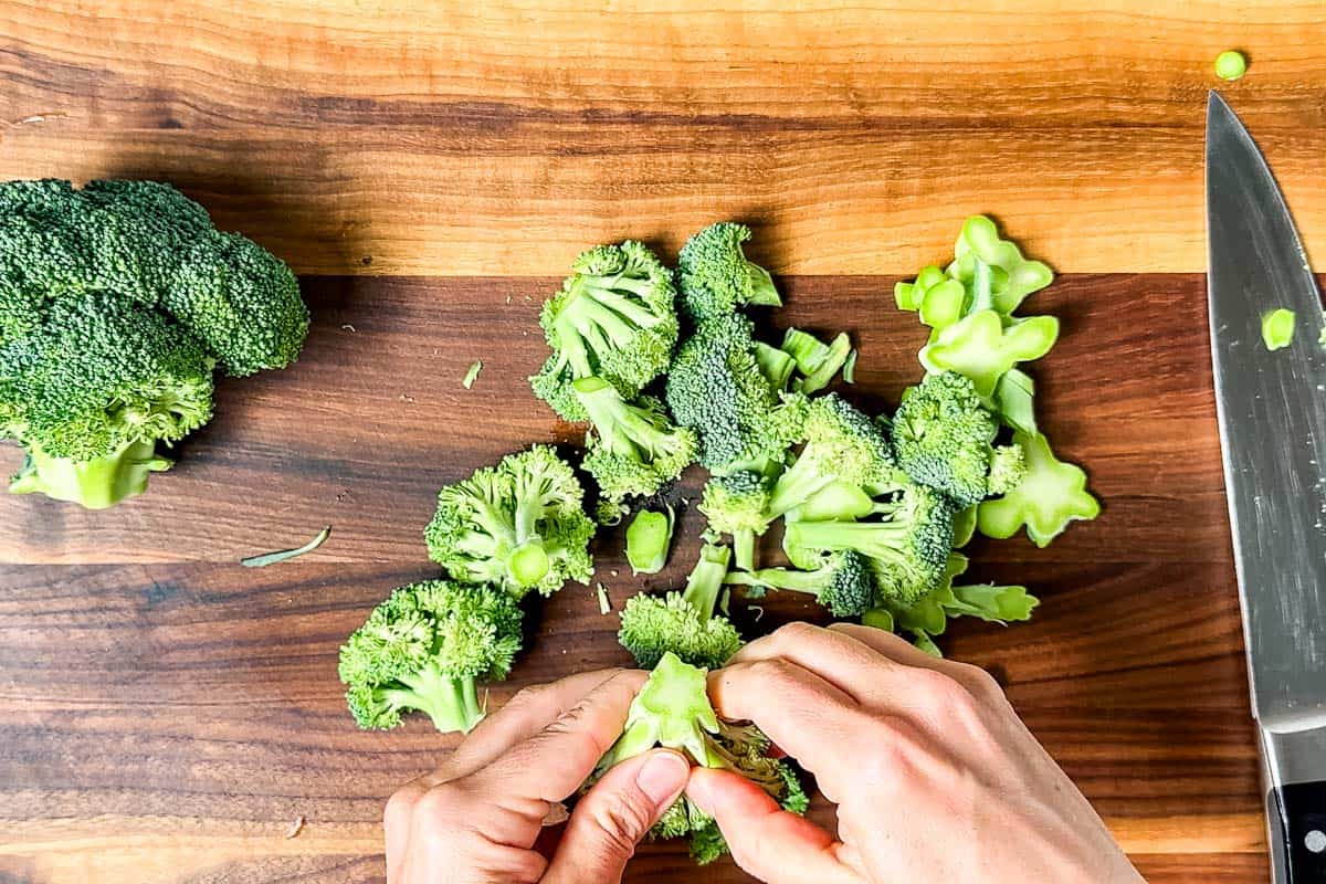 Cutting up the broccoli into small florets on a large wood cutting board.