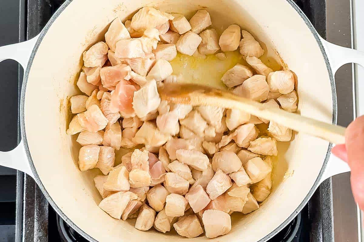 Sautéing the cubed chicken in the large white pot.