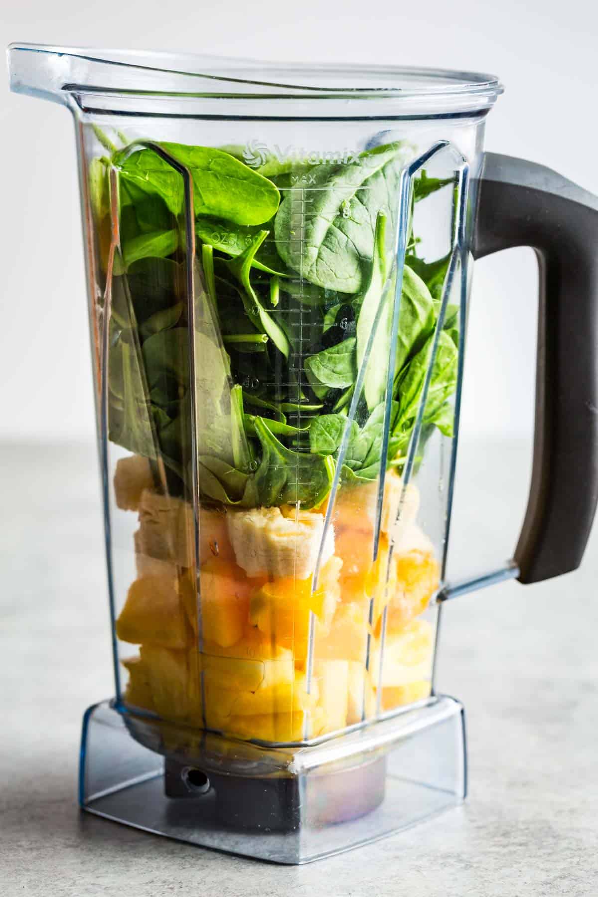 Adding the pineapple, mango, banana, and spinach to a blender container.