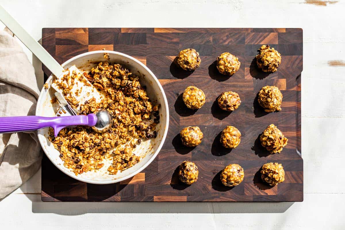 Using a cookie scoop to portion out the energy bites on a wooden cutting board.