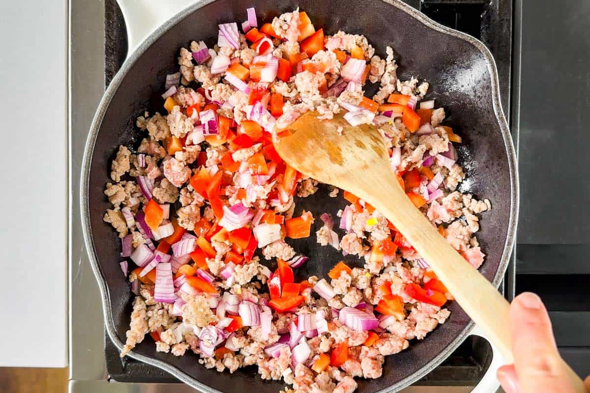 Cooking the sausage, red onion, and red bell pepper in a large white cast iron skillet.