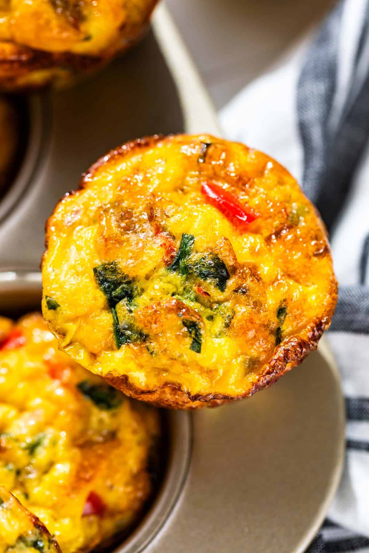 Close up of one Sausage Egg Muffins with bits of red bell pepper and spinach speckling the top of the muffin.