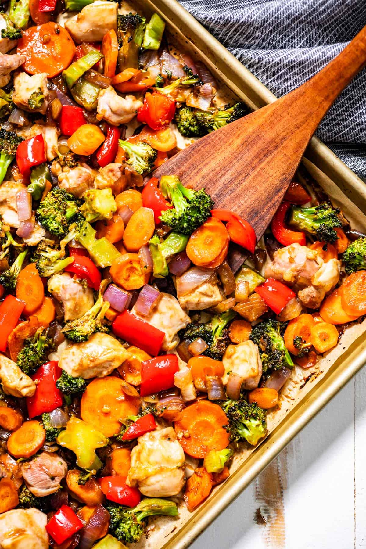 Sheet pan stir fry with a wood spatula scooping up some stir fry.