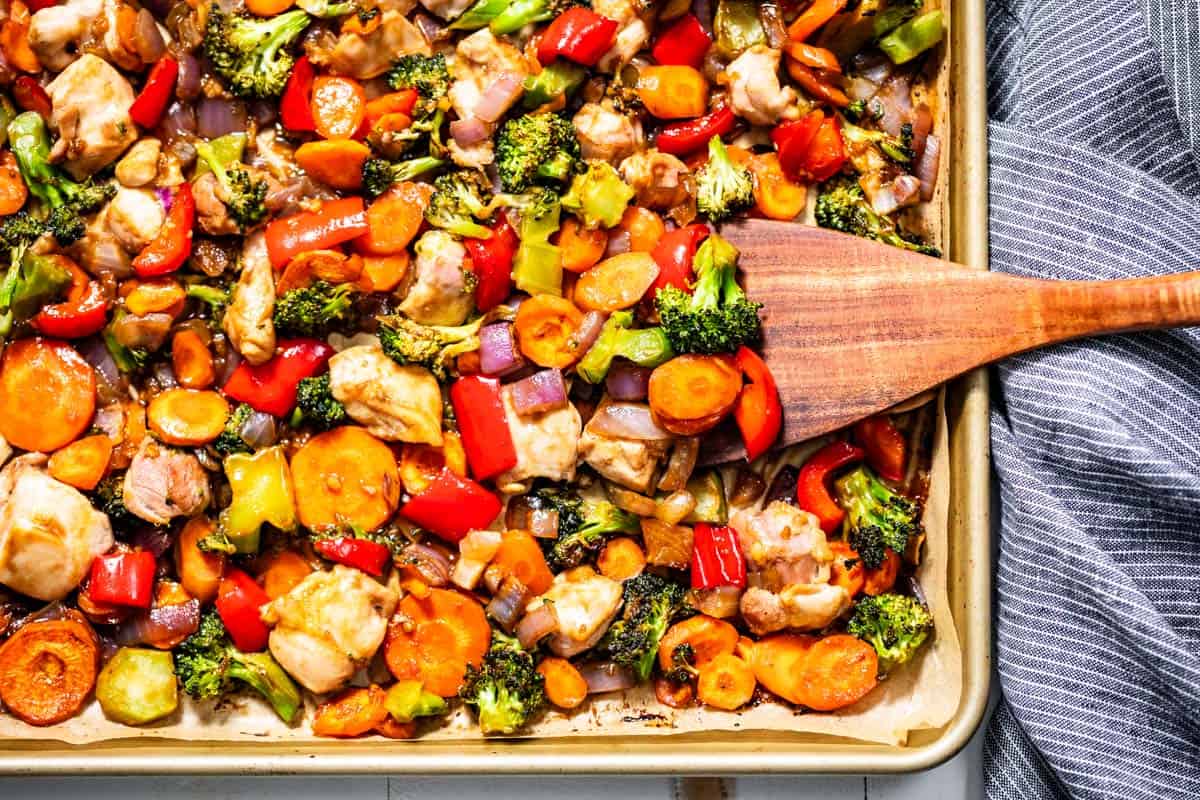 Finished sheet pan stir fry on a gold sheet pan with a wood spatula on the side.