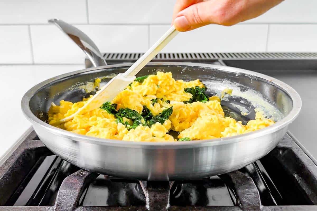 Adding the cooked spinach to the scrambled eggs.