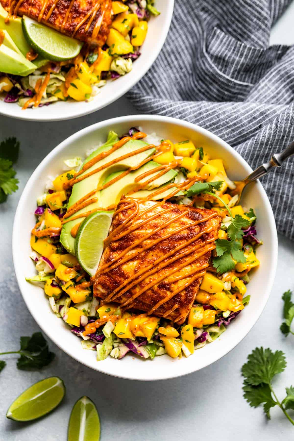 Slaw, mango salsa, and a portion of fish drizzled with chipotle aioli in a white bowl.